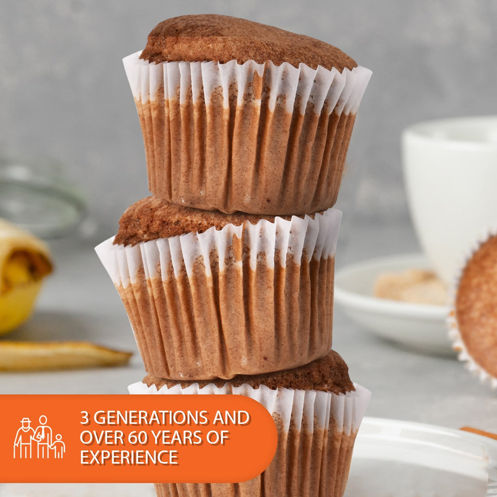 Stack of three freshly baked cappuccino muffins in white paper liners, showcasing their moist texture and golden-brown tops. Displayed on a softly blurred kitchen countertop with coffee and breakfast elements in the background, highlighting over 60 years of family baking tradition. Perfect for low-carb, sugar-free, keto-friendly breakfast, snack, dessert, or coffee break options.