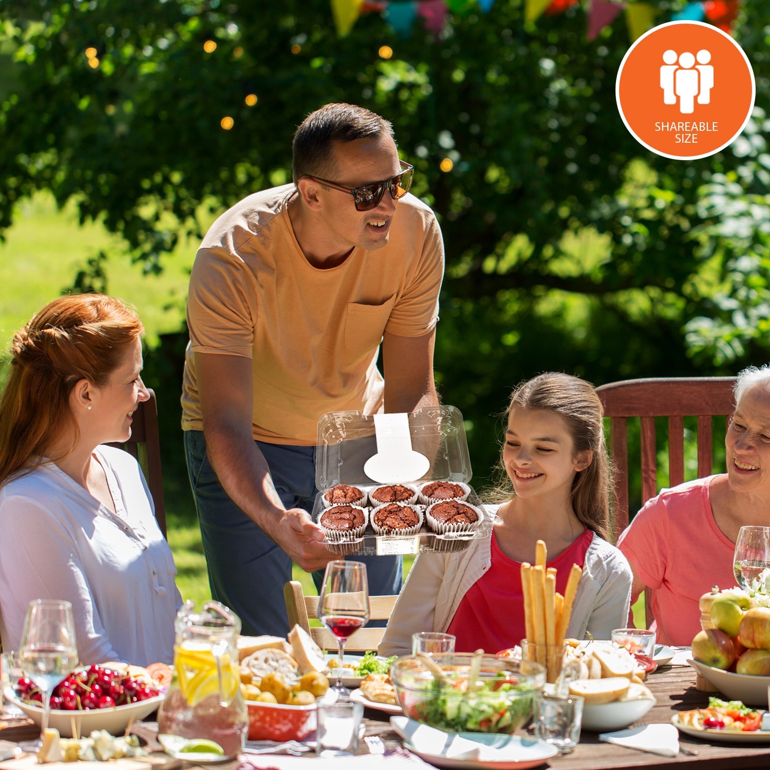 Family gathered around an outdoor table while serving fresh low-carb chocolate muffins from a bakery box, highlighting a shareable, family-size keto-friendly treat.