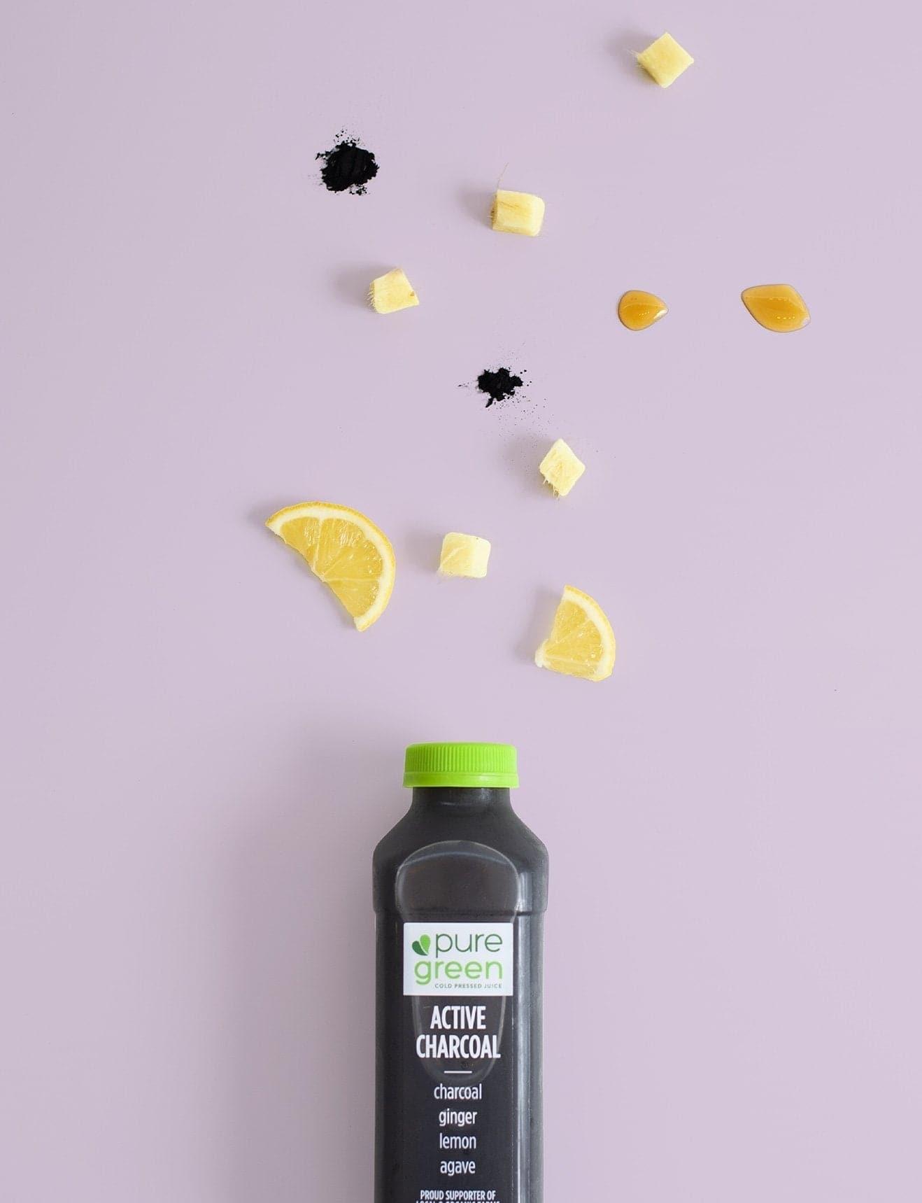 Black bottle labeled 'pure green' with a green cap on a light purple background with lemon slices. Pure Green COLD Pressed Juice. Ingredients include: Activated Charcoal, Ginger, Lemon and Agave. Kosher, NON-GMO and Gluten Free Juice Drink.