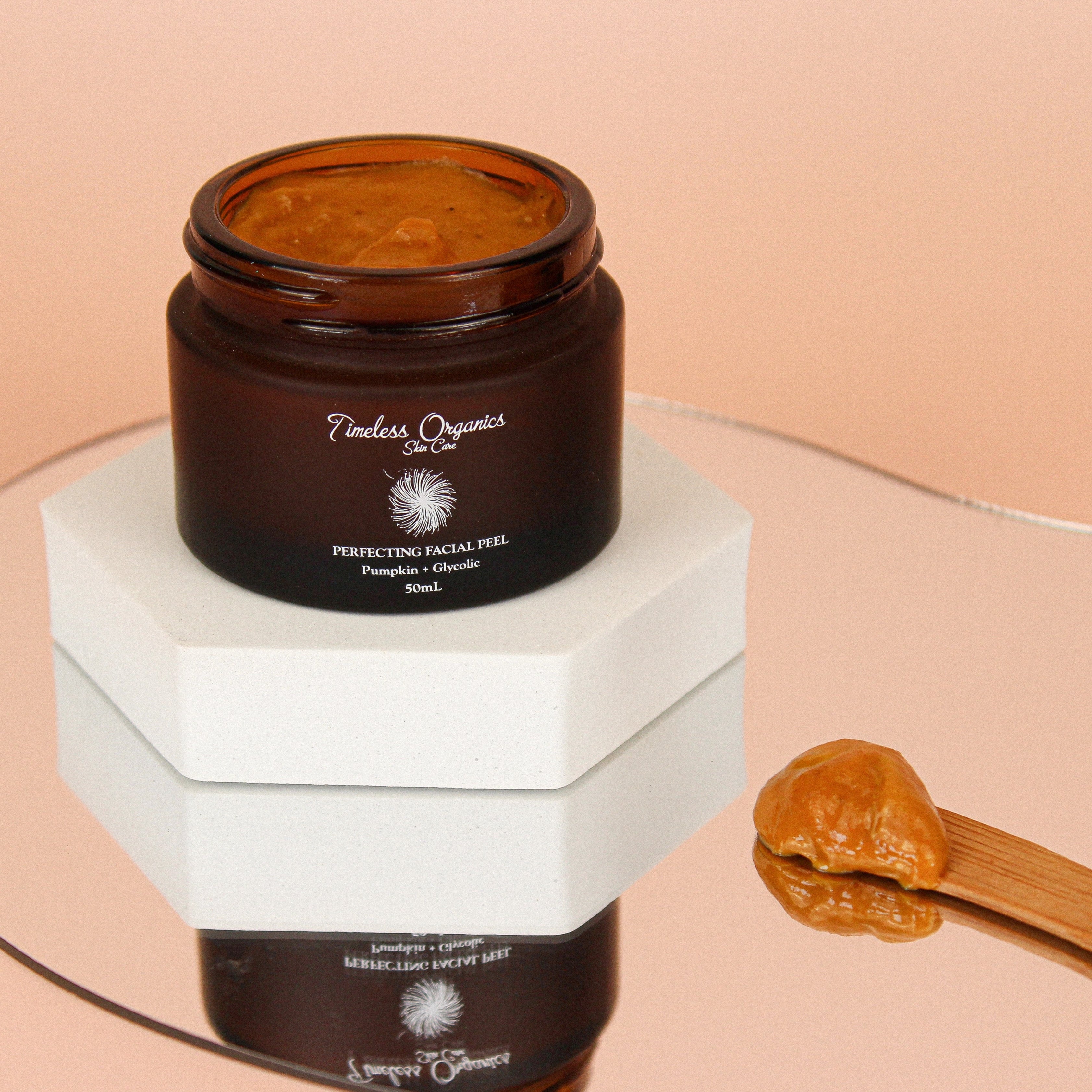 Jar of Timeless Organics facial peel with a wooden spoon on a peach background
