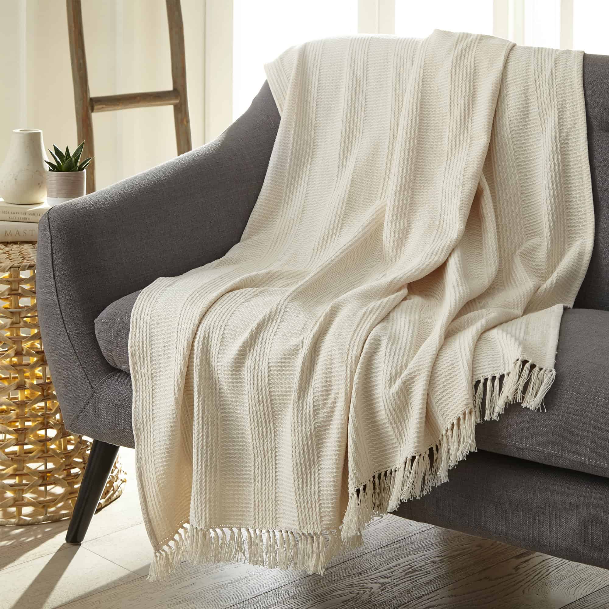 Beige textured throw blanket draped over a gray armchair in a cozy living room setting. Organic Cotton Throw with Tassels