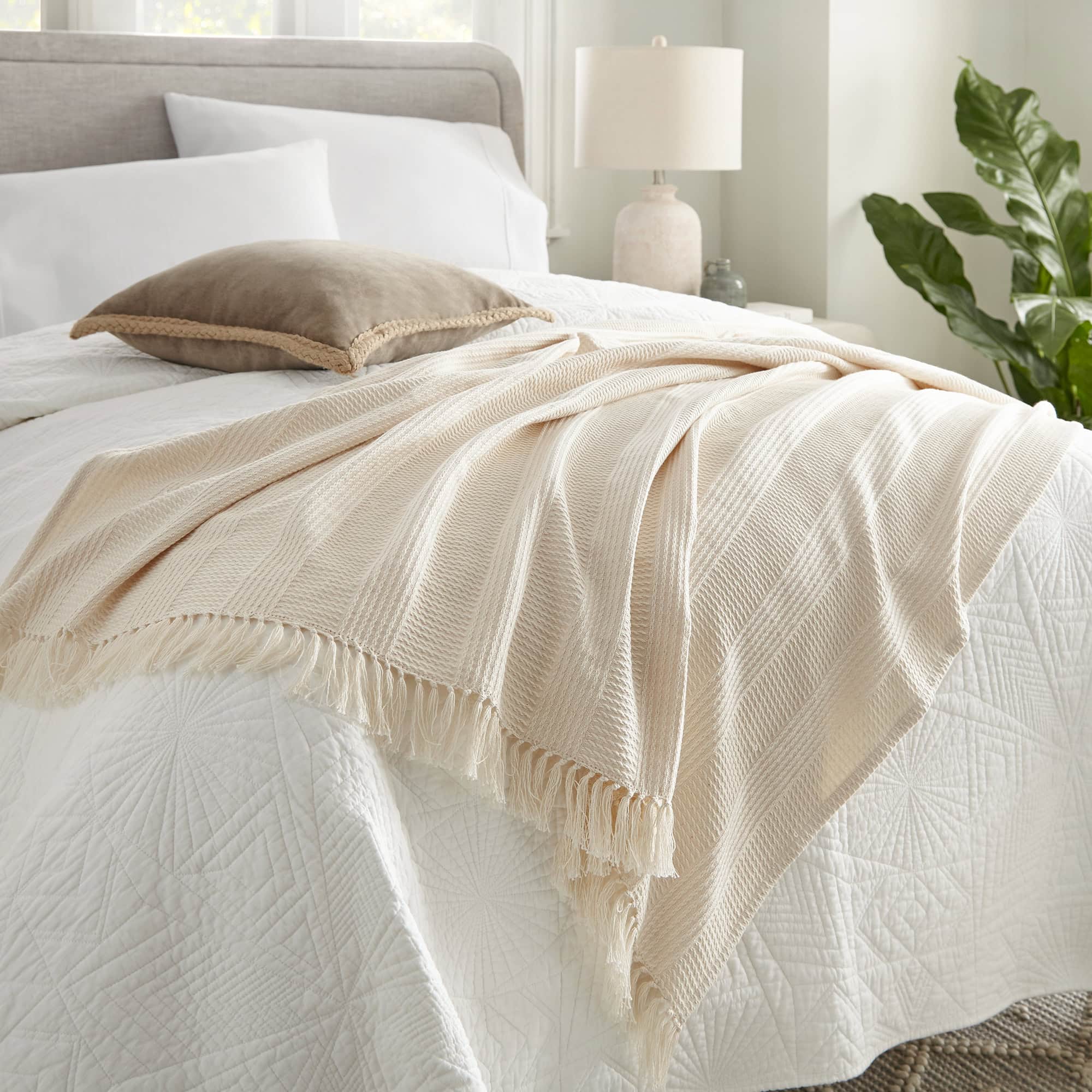Neatly made bed with beige throw blanket and pillow in a bright bedroom. Organic Cotton Throw with Tassels