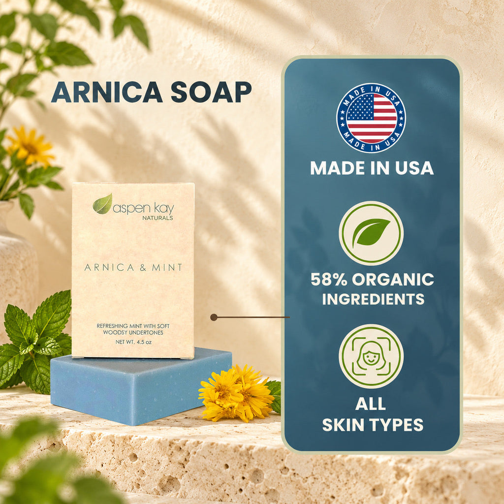 Aspen Kay Naturals Arnica & Mint soap bar displayed on a blue block next to its cream-colored packaging box, set against a warm stone background with yellow flowers and a dark blue informational badge highlighting 'Made in USA' and organic ingredients.