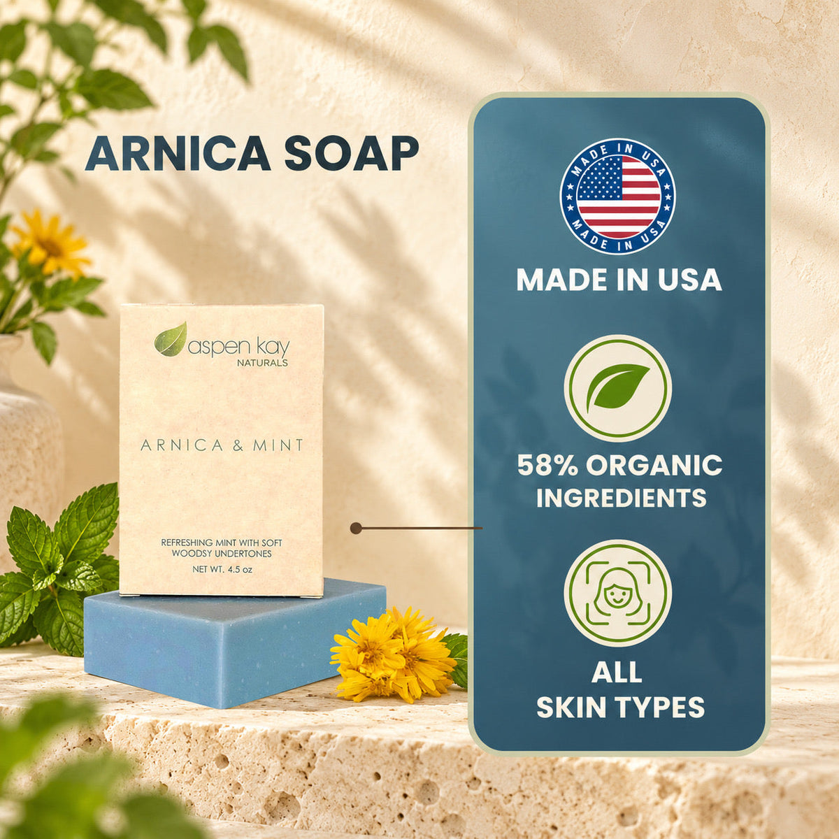 Aspen Kay Naturals Arnica & Mint soap bar displayed on a blue block next to its cream-colored packaging box, set against a warm stone background with yellow flowers and a dark blue informational badge highlighting 'Made in USA' and organic ingredients.