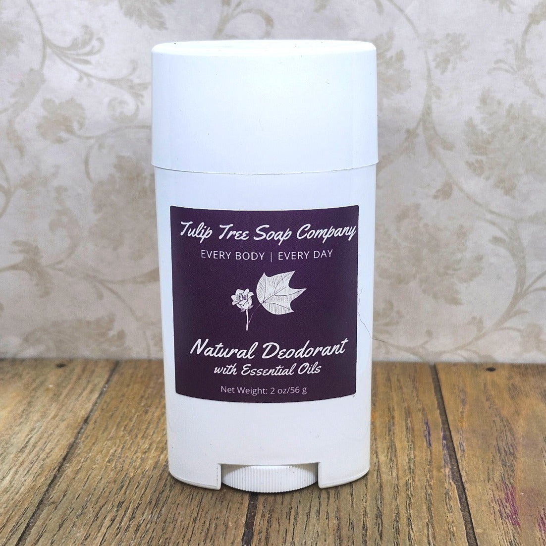 White deodorant stick with purple label on a wooden surface. Tulip Tree Soap Company. For every body. Everyday. Natural Deodorant with Essential Oils. 2 oz, 56 g Free from aluminum, baking soda, phthalates, and other harsh ingredients, this formula uses natural ingredients to neutralize odor, not just cover it up.