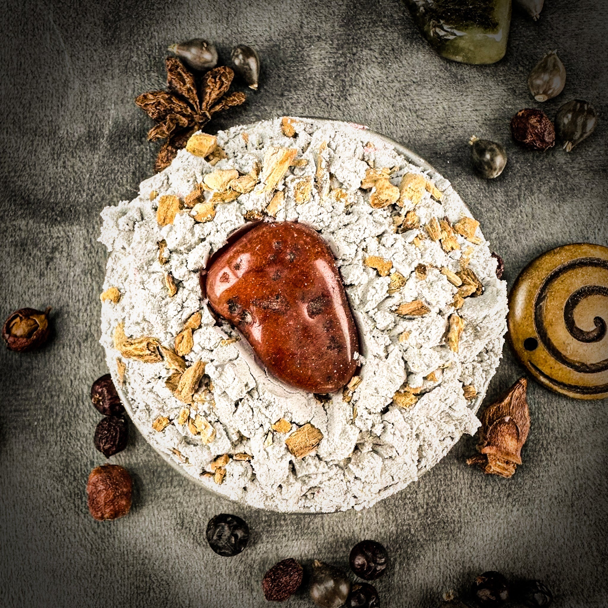 Decorative item with a central brown stone, surrounded by small stones and leaves on a textured surface. Domination Sachet Powder by Madame Pamita