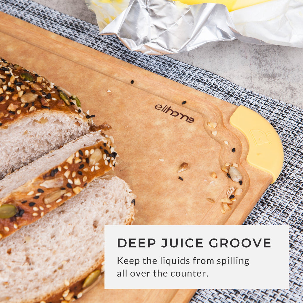 Wooden cutting board with a deep juice groove, freshly sliced artisan bread, and a yellow non-slip corner grip, designed to help contain liquids and keep kitchen countertops clean during food preparation.