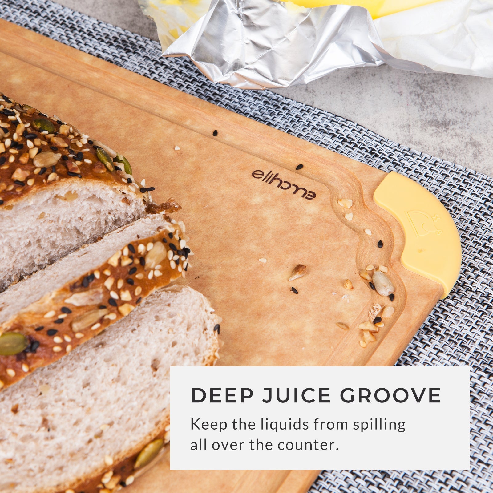 Wooden cutting board with a deep juice groove, freshly sliced artisan bread, and a yellow non-slip corner grip, designed to help contain liquids and keep kitchen countertops clean during food preparation.