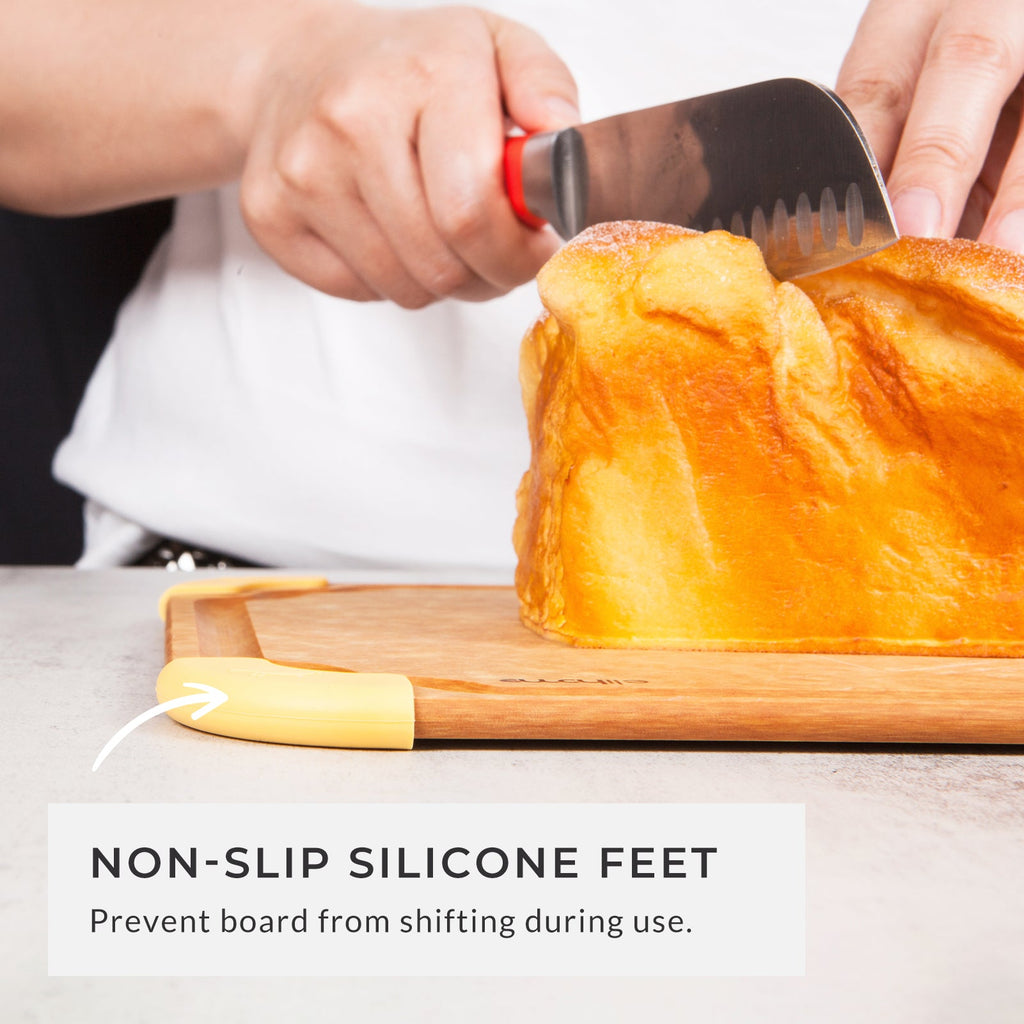 Person slicing a fresh loaf of artisan bread on a medium non-slip color-coded cutting board with silicone feet, demonstrating enhanced stability, safe food preparation, and everyday kitchen use.