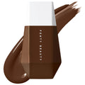 Fenty Beauty Eaze Drop Lightweight Tinted Moisturizer bottle with rich deep brown shade and matching foundation swatches on a white background.