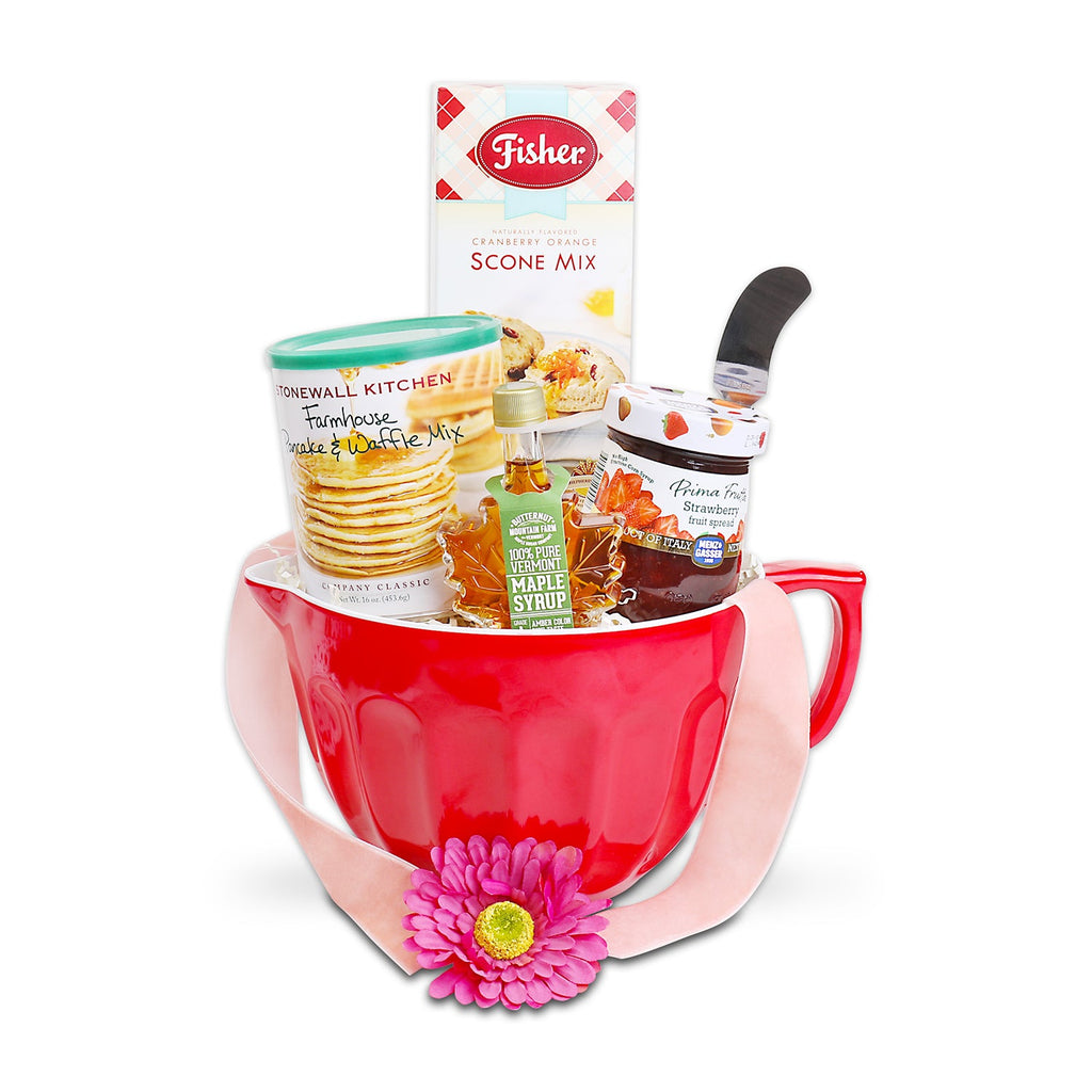 Home Made Morning Baking Gift Basket featuring a red ceramic mixing bowl filled with gourmet breakfast favorites including pancake and waffle mix, cranberry orange scone mix, strawberry preserves, pure Vermont maple syrup, honey, a spatula, and a decorative pink flower. Home Made Morning Baking Gift Basket: Vermont Maple Syrup, Pancake &amp; Waffle Mix, Fisher Original Fair Scone &amp; Shortbread Mix, Fresh Fruit Jam, Stainless Steel Spread Knife, Red Mixing Bowl with Handle