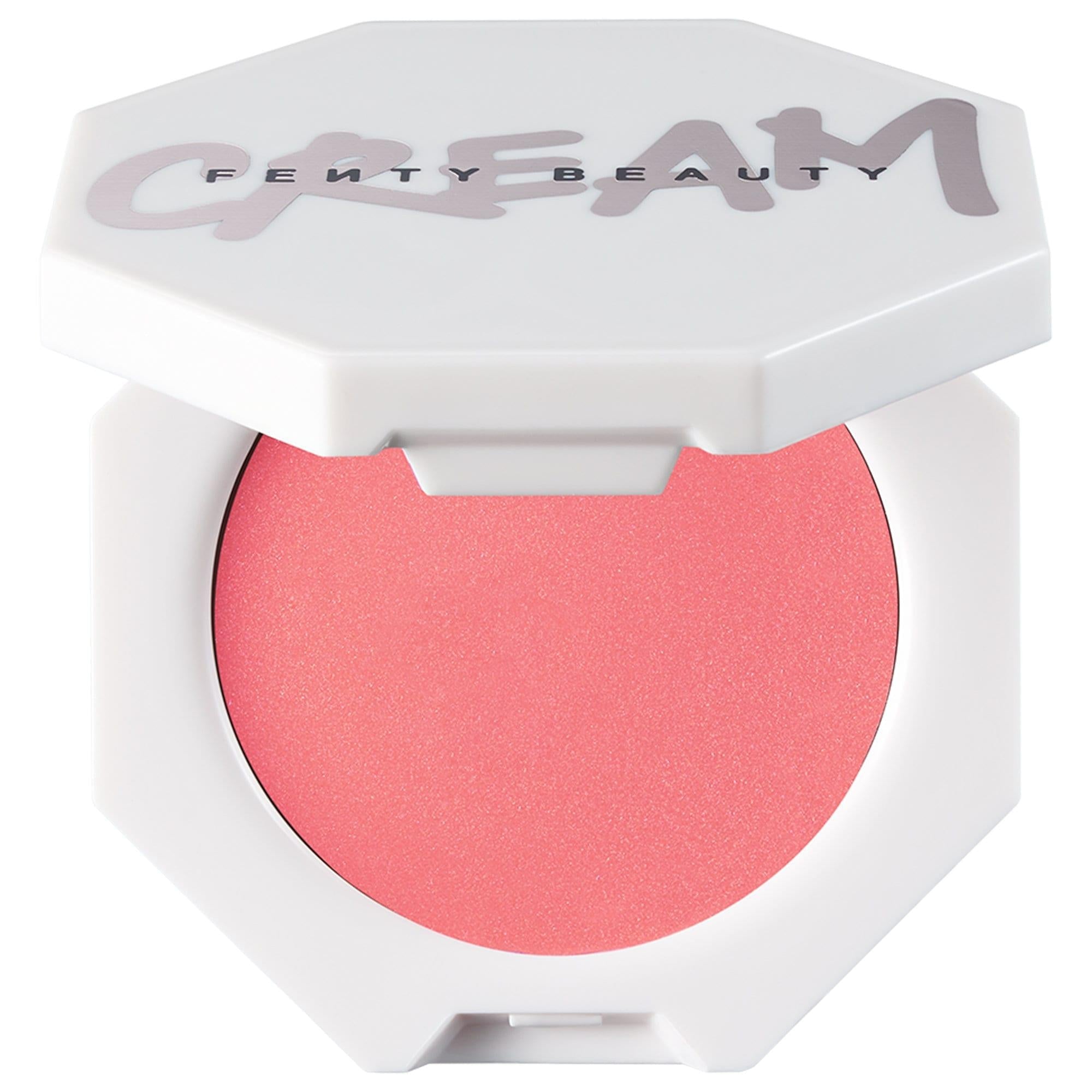Fenty Beauty Cheeks Out cream blush in a white hexagonal compact with the lid open, revealing a vibrant coral-pink cream blush and the Fenty Beauty logo on the lid.