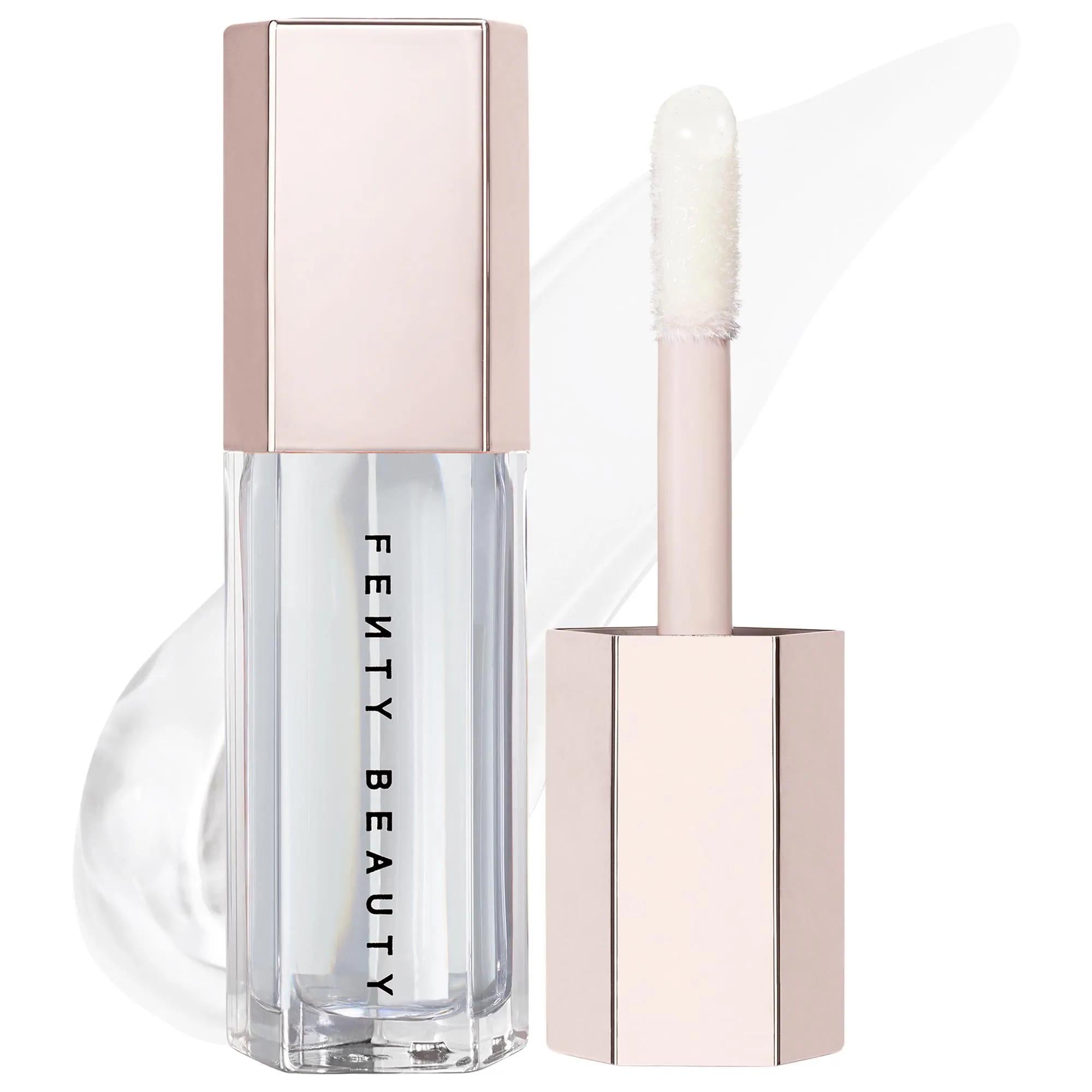 Fenty Beauty Clear Lip Tint in a clear bottle with a pale pink cap, shown next to its applicator wand on a white background with a soft pink smear. Fenty Beauty Gloss Bomb: Universal Lip Luminizer - Explosive Shine, Hydrating & Non-Sticky Formula for All Skin Tones