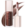 Fenty Beauty liquid lipstick in a metallic bronze-brown shade, shown with the cap off and the applicator wand against a white background with a matching product smear. Fenty Beauty Gloss Bomb: Universal Shine Lip Luminizer - Non-Sticky, Hydrating Peach Vanilla Lip Gloss for All Skin Tones