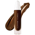 Fenty Beauty Pro Filt'r Soft Matte Longwear Liquid Foundation in a frosted glass bottle with a white cap, displayed in front of a rich brown foundation swatch on a clean white background. Long-wear, soft matte liquid foundation for buildable medium-to-full coverage.