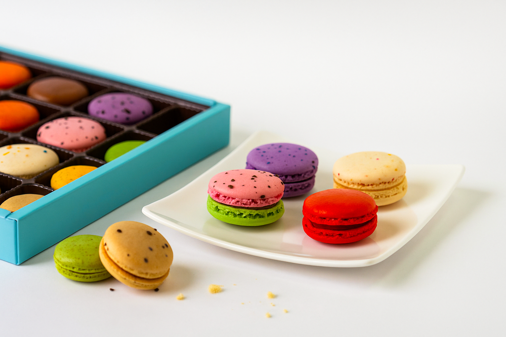 Colorful macarons on a white plate with a box of macarons in the background.