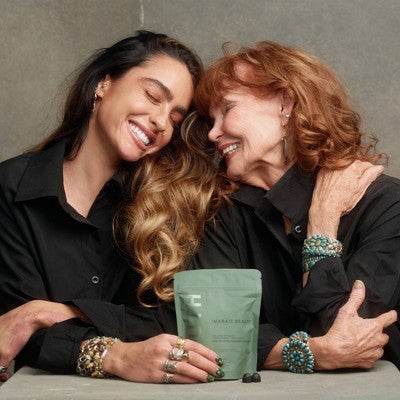Two women hugging with a green package between them on a neutral background