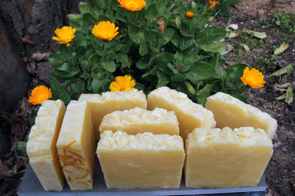 Blocks of soap with a natural, textured surface on a stone surface with flowers in the background.