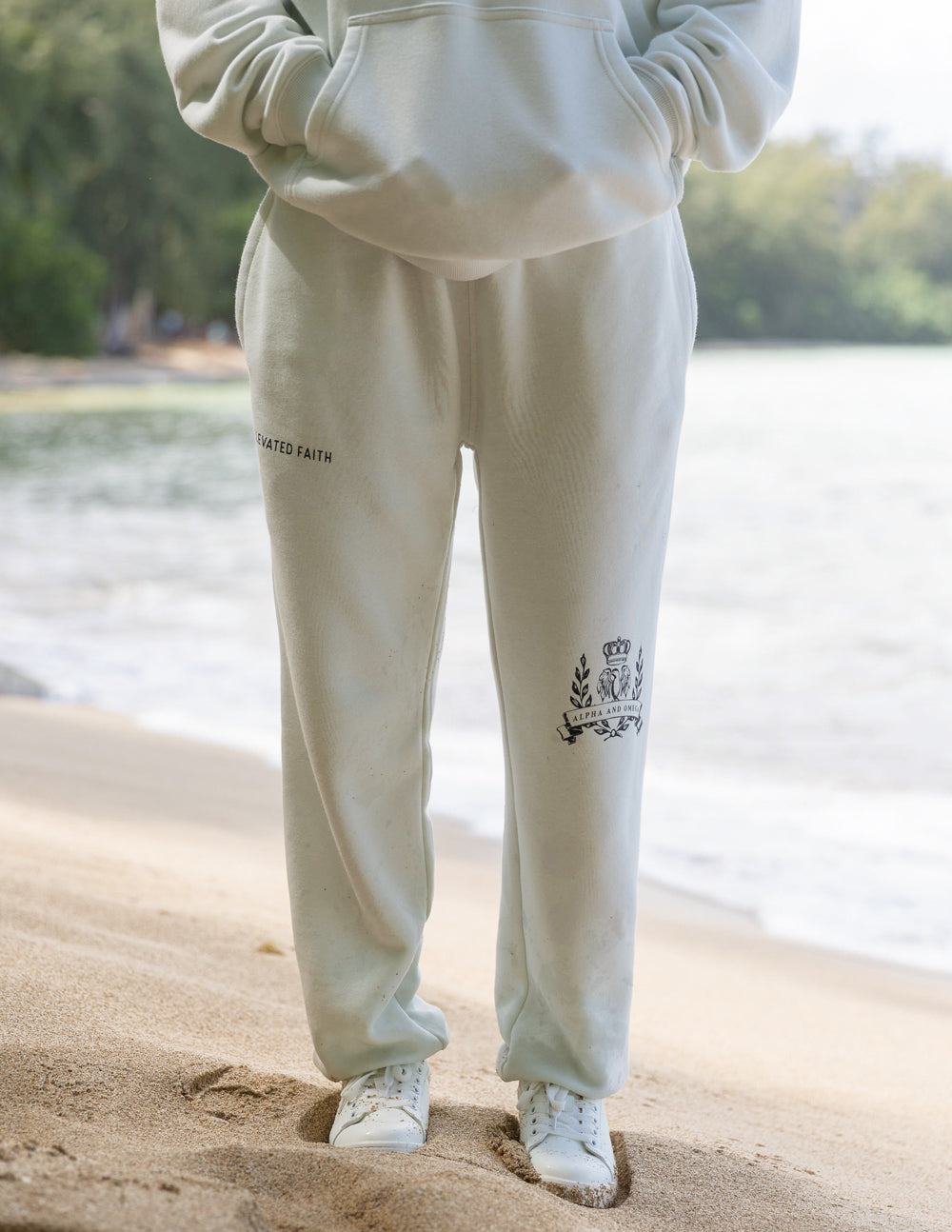 Person wearing a light-colored tracksuit with logos on the beach