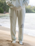 Person wearing a light-colored tracksuit with logos on the beach