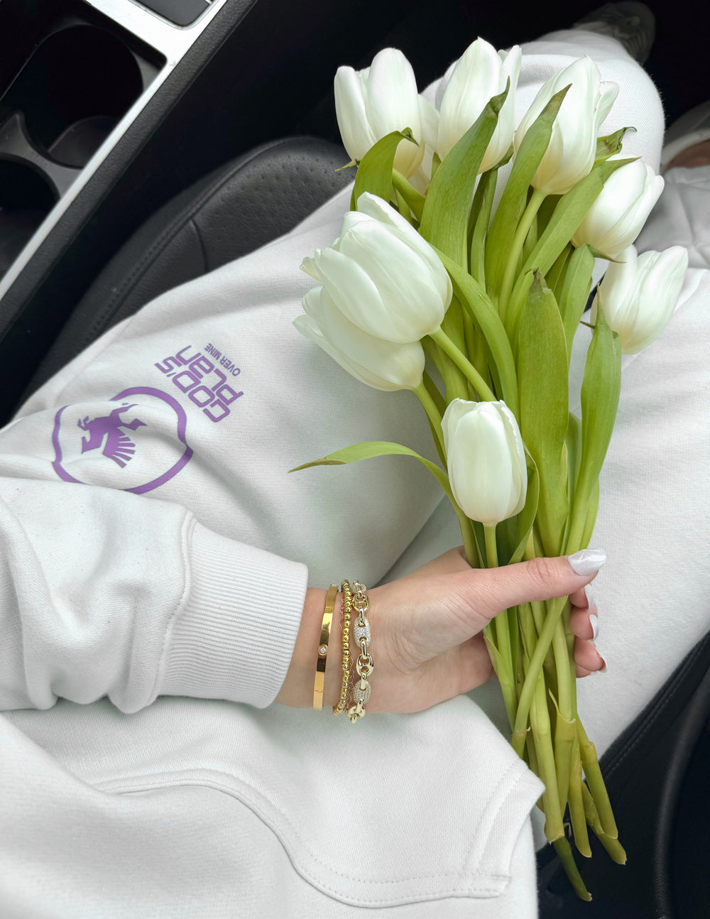 Person holding a bouquet of white tulips with a branded sweatshirt in the background