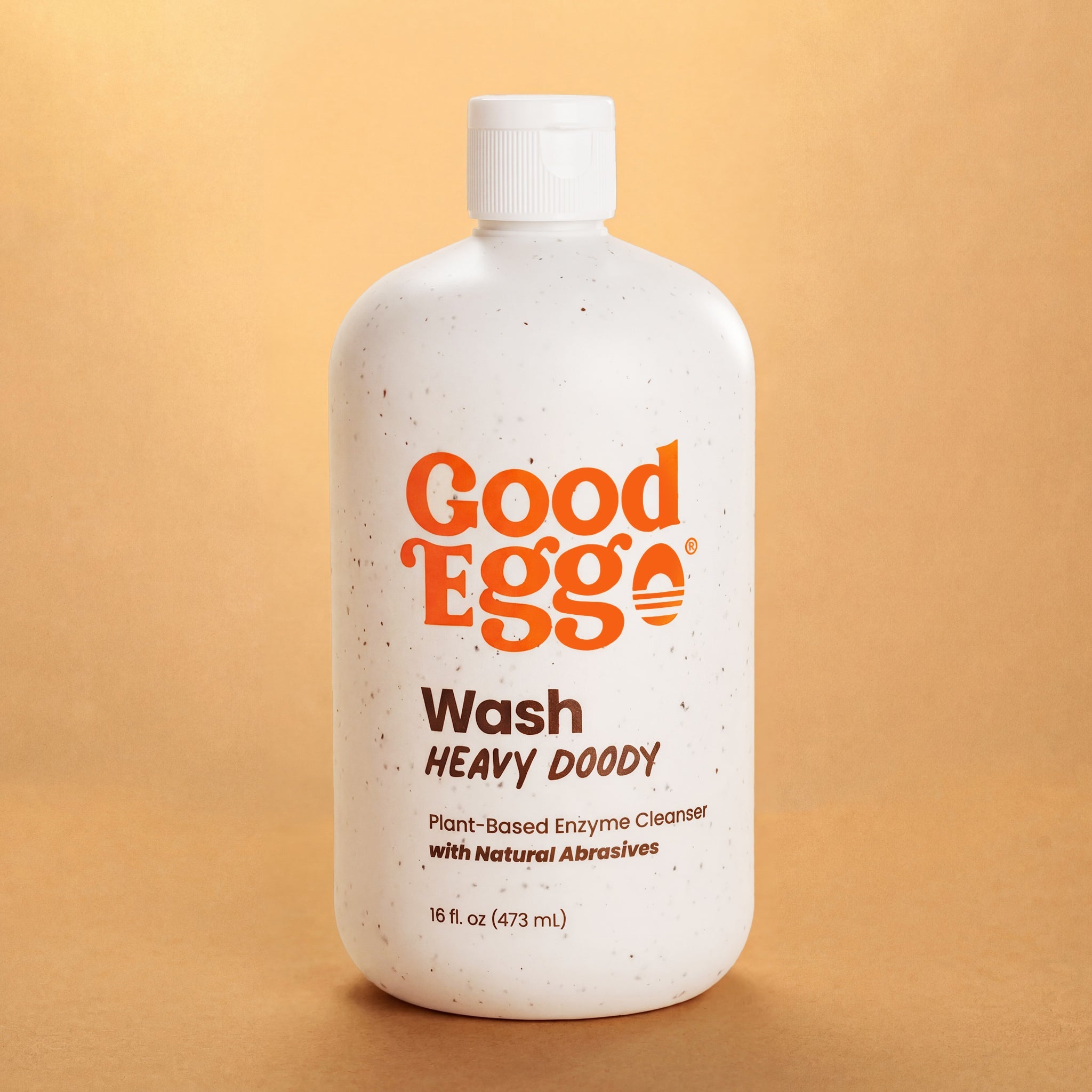 A 16 fl oz bottle of Good Egg Wash Heavy Doody plant-based enzyme cleanser, featuring a white speckled bottle with orange and brown text, set against a warm tan background.