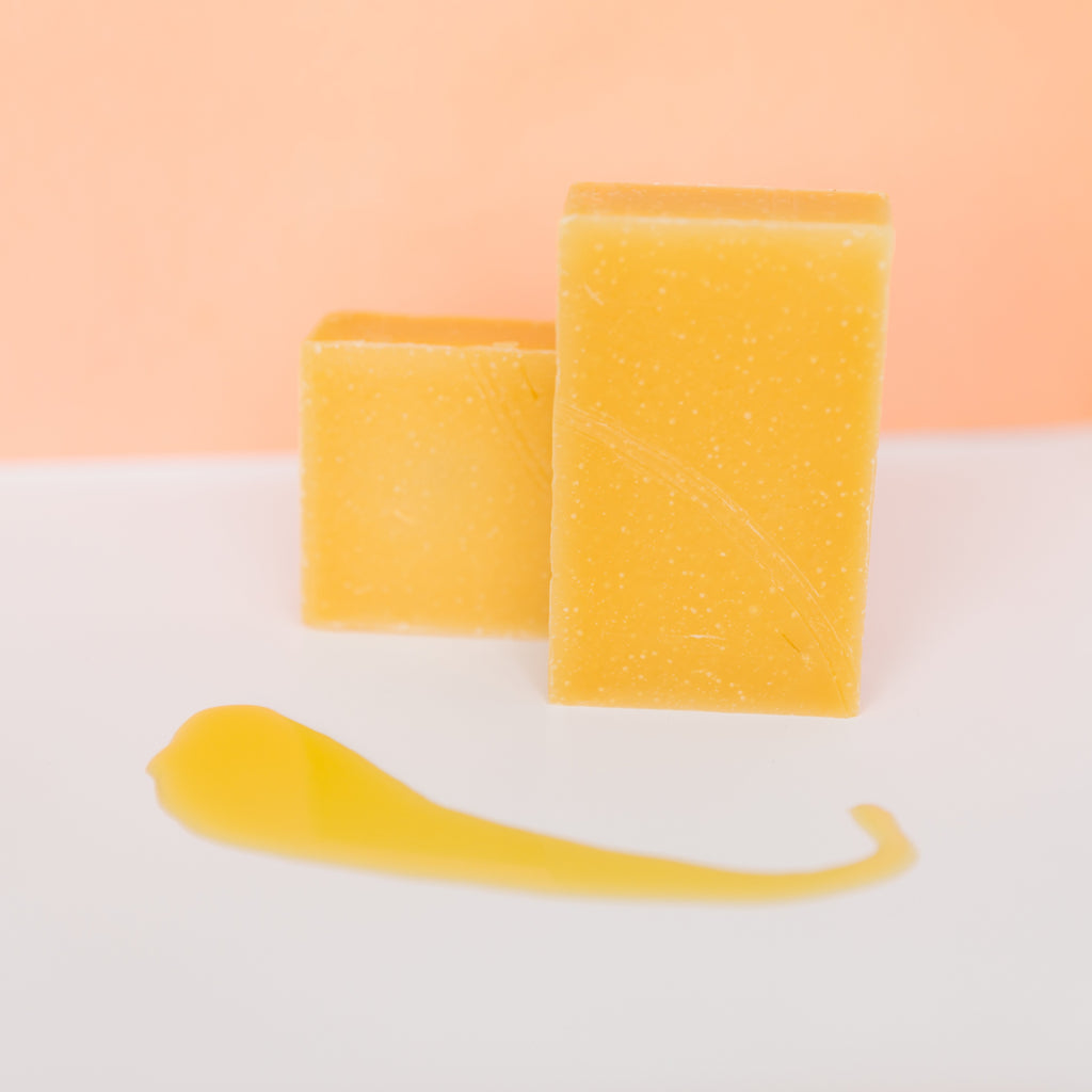 Two yellow sponges and a yellow tool on a white surface with a peach-colored background