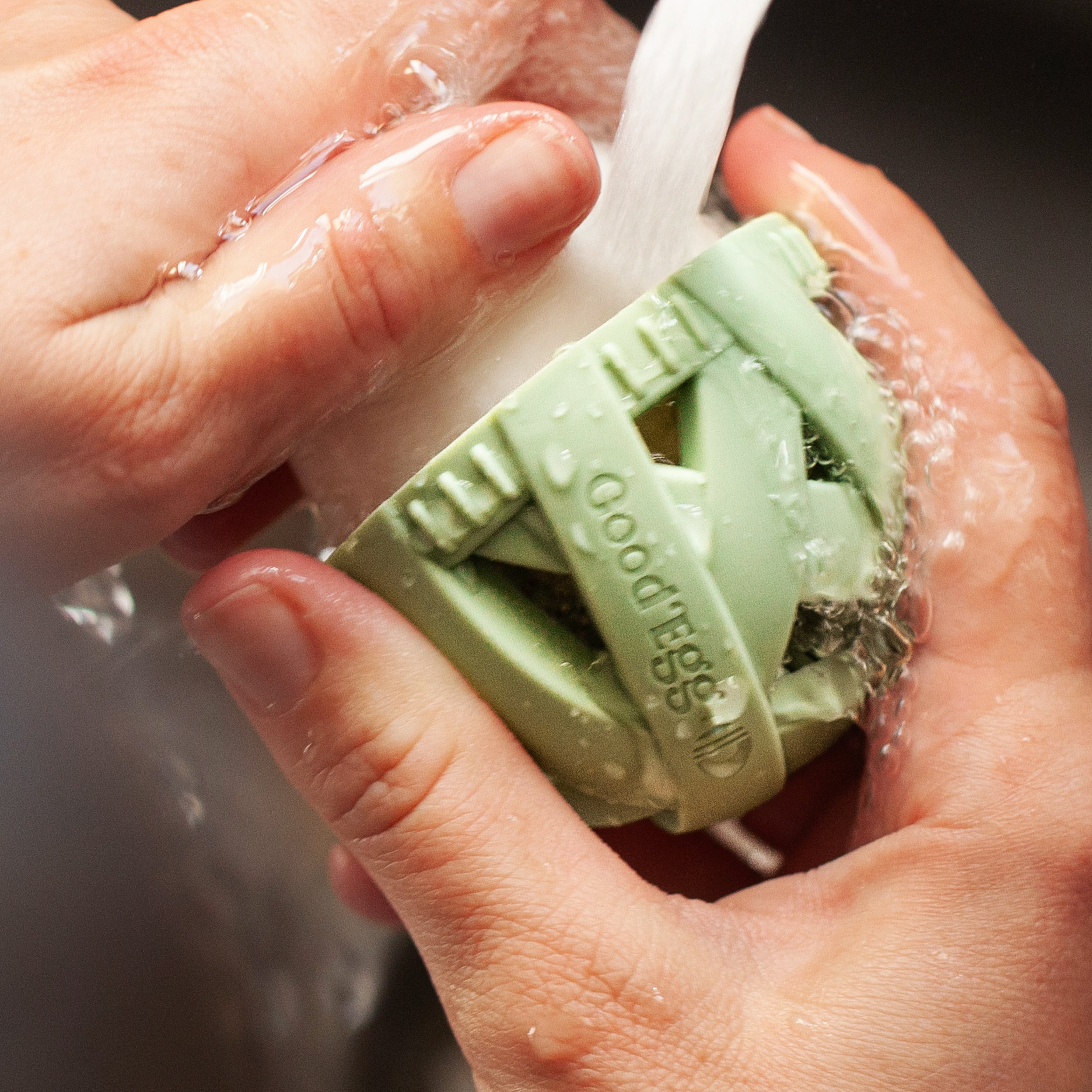 Person rinsing a fresh egg under running water using a mint green GoodEgg silicone egg cleaning brush, highlighting the flexible scrubbing nubs, ergonomic grip, and gentle cleaning action for cleaning farm-fresh chicken, duck, goose, and backyard poultry eggs.