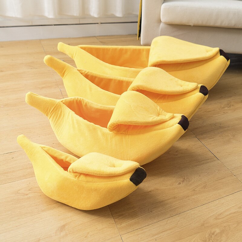 Yellow banana-shaped pet bed on a wooden floor, featuring a soft plush design with a cozy hooded opening for cats and small dogs.