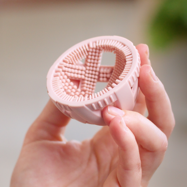 Hand holding a blush pink GoodEgg silicone egg cleaning brush with flexible scrubbing nubs, showcasing the ergonomic design for gently cleaning fresh chicken, duck, and jumbo eggs.
