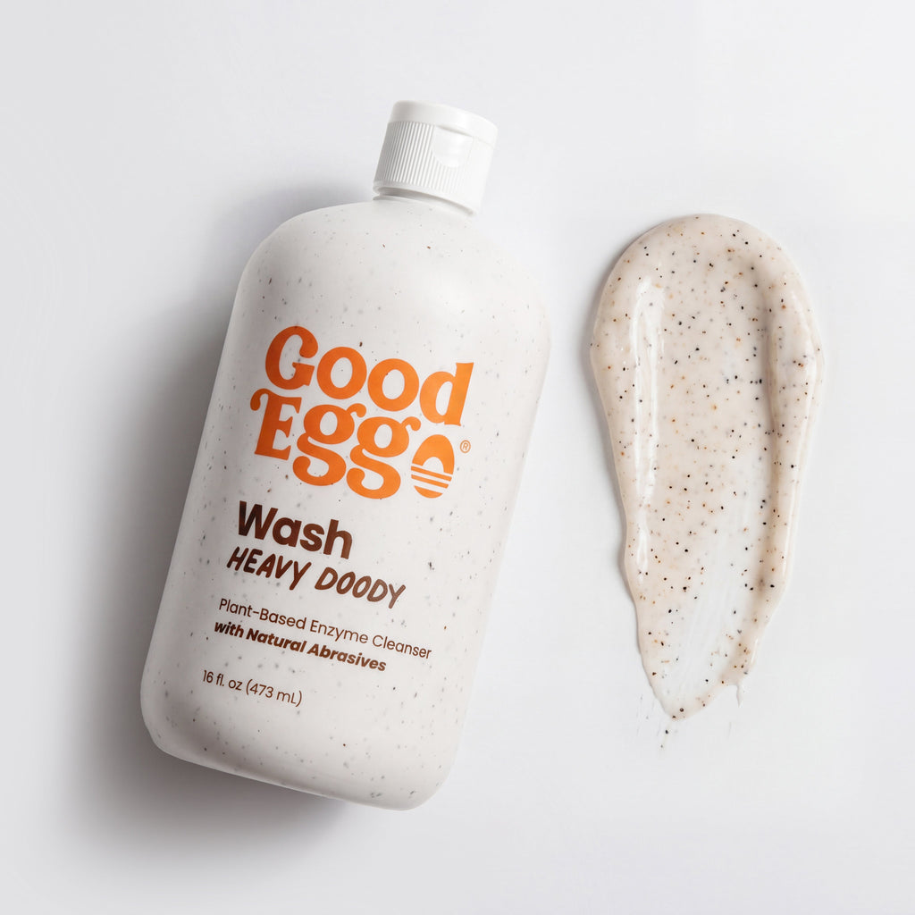 A bottle of Good Egg Wash Heavy Doody plant-based enzyme cleanser with orange branding, shown next to a smear of the thick, speckled cream cleanser on a clean white background.