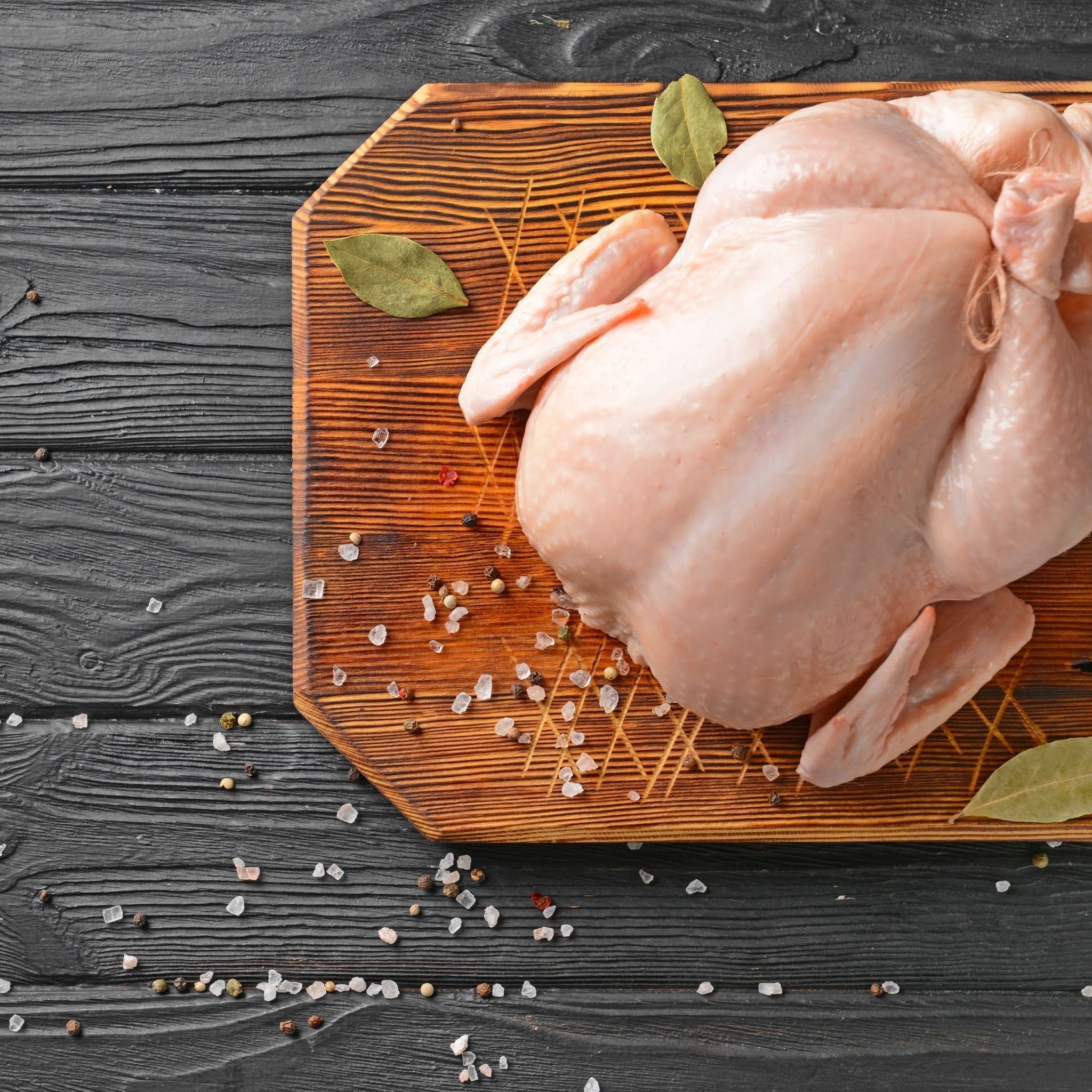 Raw USDA Certified Organic whole chicken, vacuum-sealed and pasture-raised by Hendricks Farm & Hatchery. Non-GMO and soy-free, shown tied with butcher's twine on a wooden cutting board with bay leaves, coarse salt, and peppercorns, photographed from above.