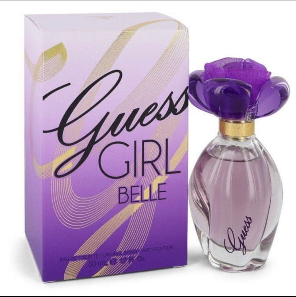 Guess Girl Belle perfume bottle and its packaging box. The bottle features a purple flower-shaped cap and a gold collar, while the box is purple with gold wavy lines and black lettering.