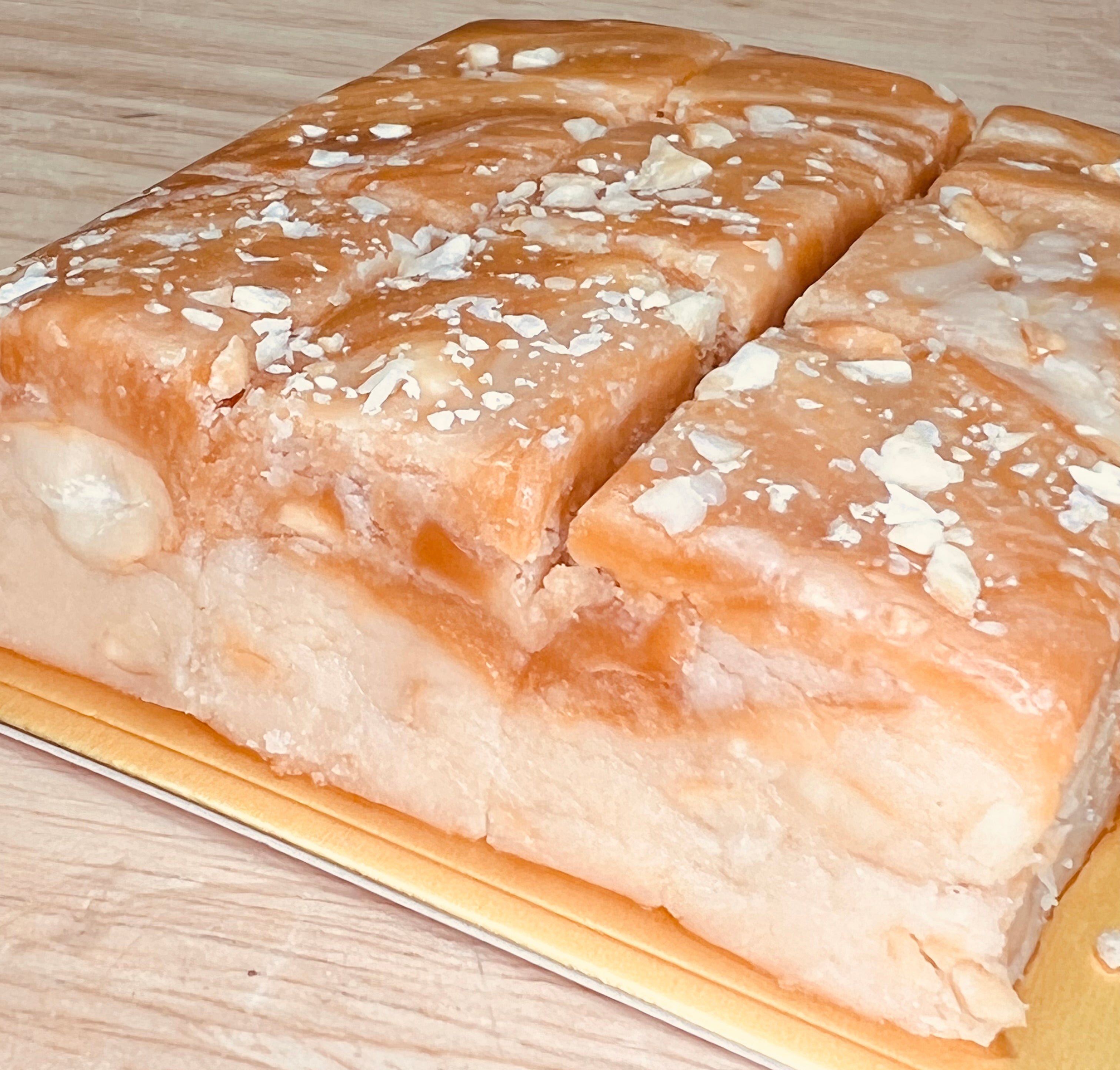 Handmade salted caramel cashew fudge slab sliced into generous squares, topped with chopped cashews and a smooth caramel glaze, displayed on a wooden cutting board over a light wood surface.