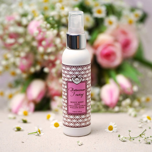 Buttercream Frosting Hydrating Body Mist bottle with organic aloe and willow bark surrounded by soft pink flowers on a floral background. Buttercream Frosting Hydrating Body Mist with Organic Aloe & Willow Bark bottle displayed with a soft floral background, featuring a moisturizing vanilla gourmand body mist with organic aloe and willow bark.