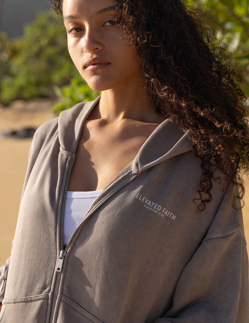 Woman wearing a gray hoodie with 'Elevated Faith' branding outdoors.