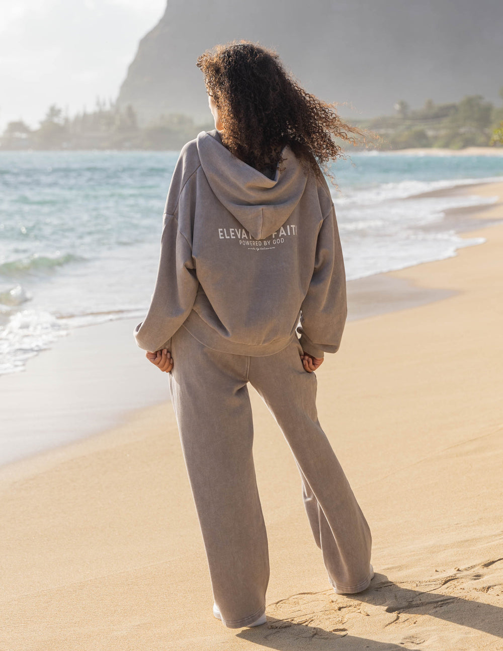 Person wearing a beige hoodie and pants on a beach with 'Elevate Your Self' text.