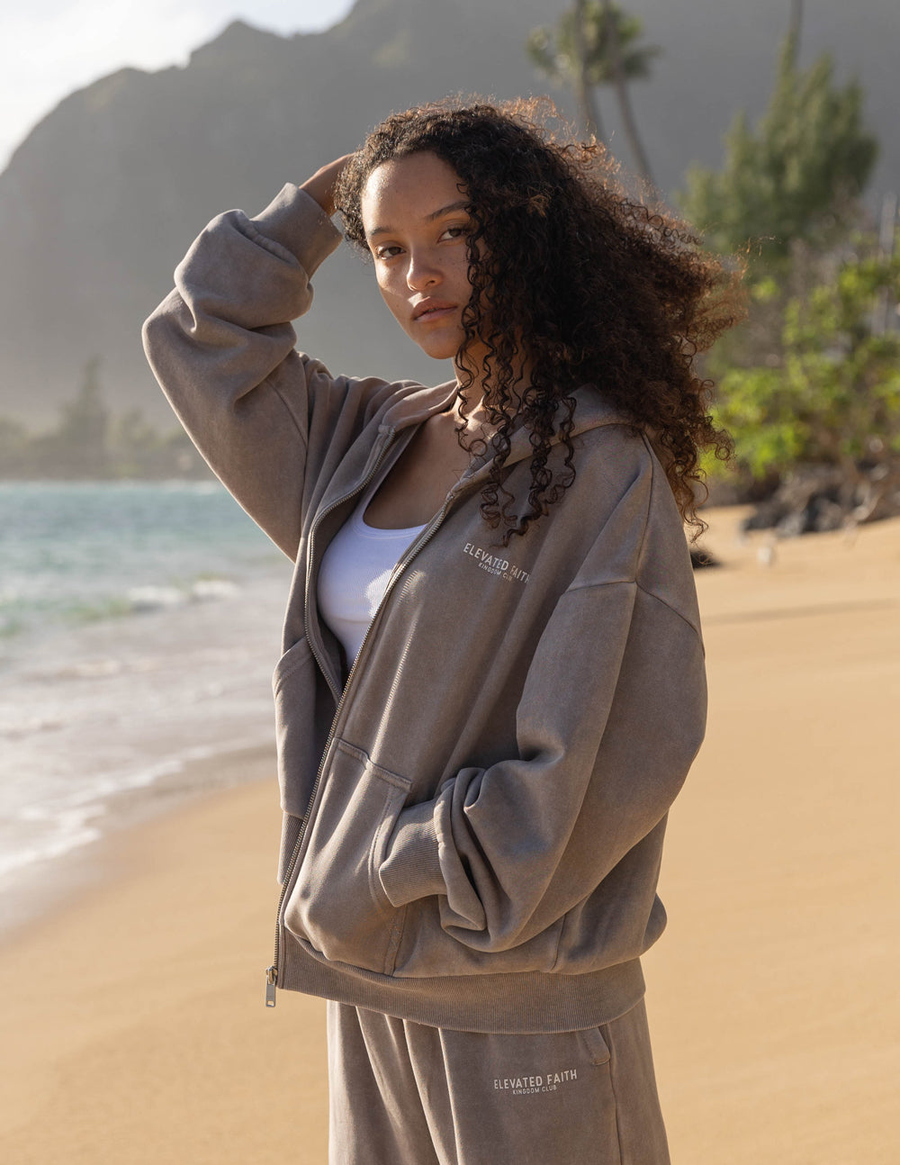 Woman wearing a gray tracksuit on a beach with mountains in the background