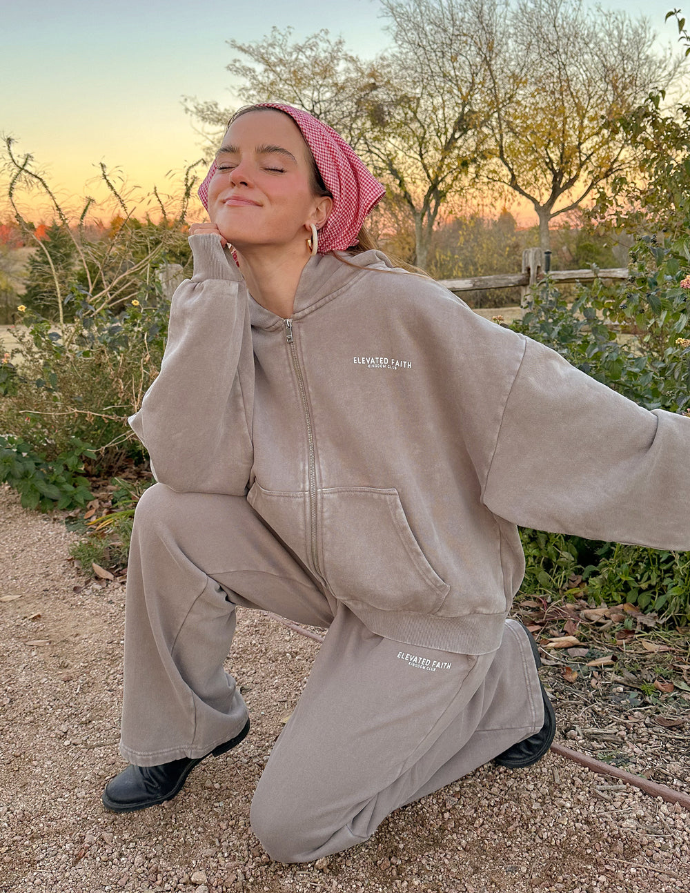 Person wearing a beige tracksuit with 'Supreme' logo outdoors during sunset.