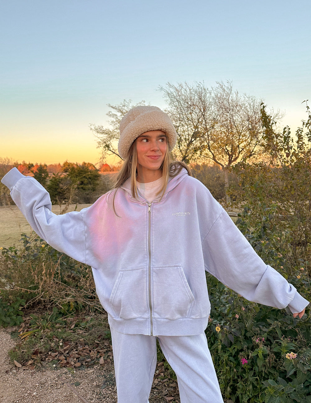 Person wearing a white hoodie and pants with a beanie outdoors during sunset.