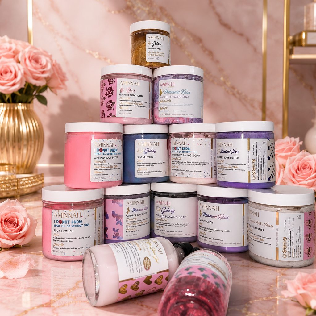 Luxury AMINNAH clean beauty skincare and body care collection displayed in an elegant pyramid on a pink marble countertop with blush roses and gold décor, featuring **vegan, cruelty-free, paraben-free, gluten-free** products made with **natural ingredients** in **recyclable packaging**. Premium self-care gift set from a **female-owned brand**, perfect for luxury skincare, spa gifts, and conscious beauty enthusiasts.
