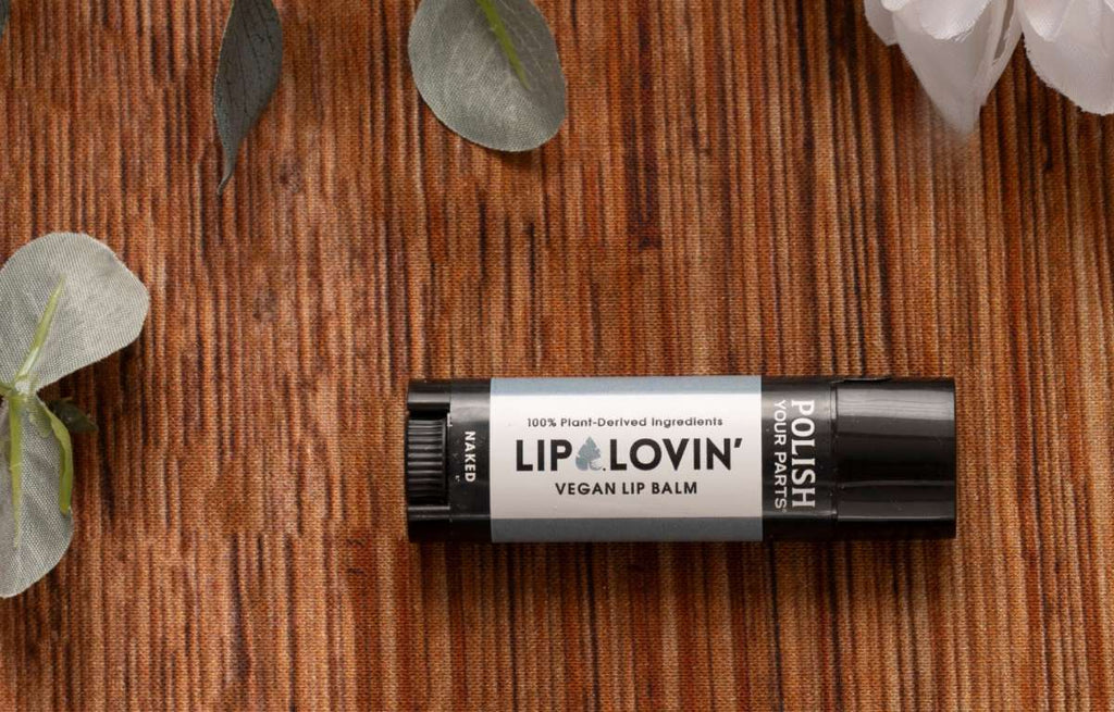 Lip Lovin’ Vegan Lip Balm in Naked, 100% plant-derived lip care with nourishing botanical ingredients, moisturizing vegan lip balm for soft smooth hydrated lips, natural cruelty-free lip care, clean beauty self-care essential, minimalist black tube on warm wooden surface with delicate leaves, Tree of Life Grocers.
