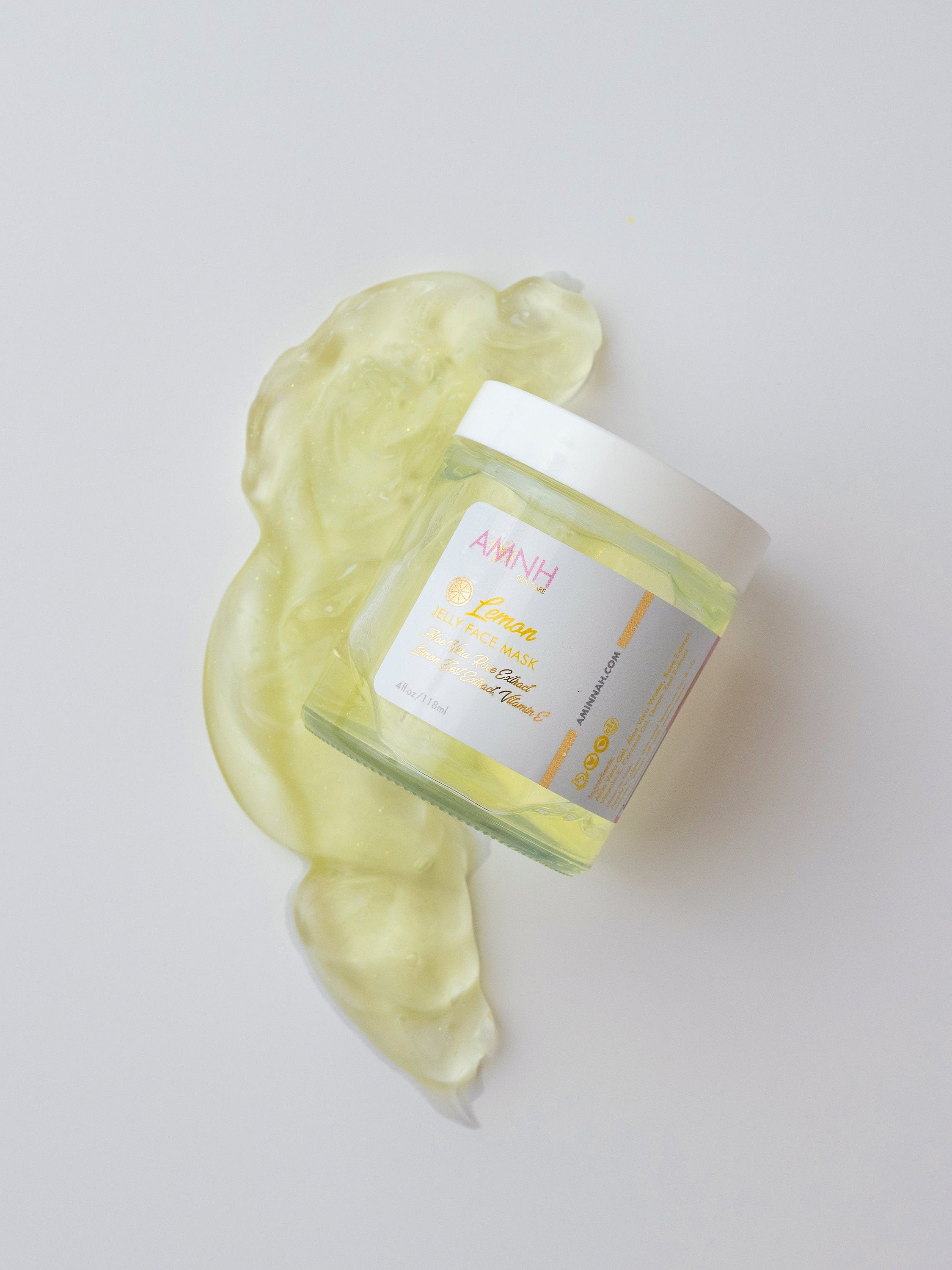 AMINNAH Lemon Jelly Face Mask in clear jar with bright yellow jelly texture spread on white background. Hydrating vegan face mask made with aloe vera, lemon zest extract, rose extract, coconut oil, and vitamin E. Cruelty-free clean beauty skincare from a female-owned brand.