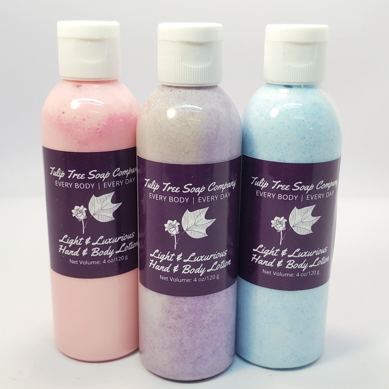 Three bottles of Tulip Tree Soap Company hand and body lotion in pink, purple, and blue on a white background. Unique blend of sunflower oil, avocado oil, and vitamin E with just a touch of cocoa butter. A light, quick-absorbing lotion that hydrates, nourishes, and soothes dry skin without leaving you feeling greasy! Plus, paraben-free, phthalate-free, good for sensitive skin.