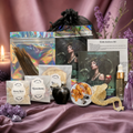 A styled product display of a 'Kith Goddess Kit' containing various ingredients and accessories, including raw rose petals, cinnamon sticks, dried herbs, a black apple, crystals, and a small glass bottle, arranged on a draped mauve satin fabric with purple flowers and a lit candle. Metaphysical items. Lilith Devotional Goddess Kit with orris root, rosebuds, incense sticks and oil for evoking Lilith: Goddess of independence, sexuality, feminine sovereignty, and righteous rage. Dark feminine occult work.