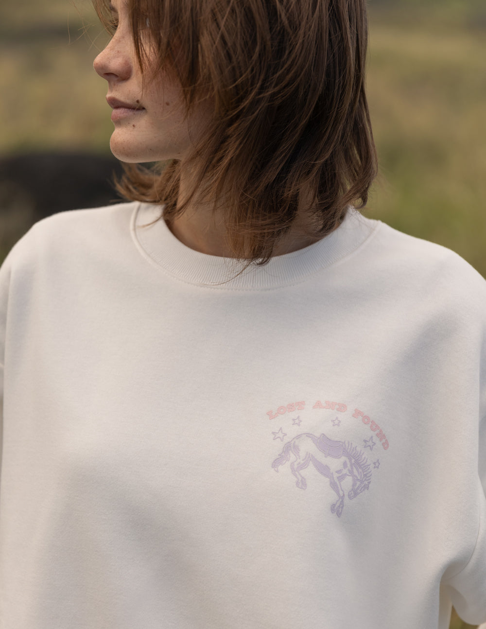 Person wearing a white sweatshirt with a horse graphic and text in a natural setting