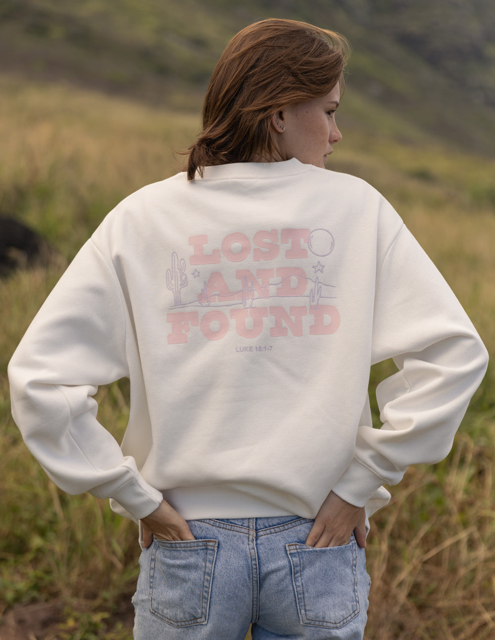 Person wearing a white sweatshirt with 'Lost and Found' text in a natural setting