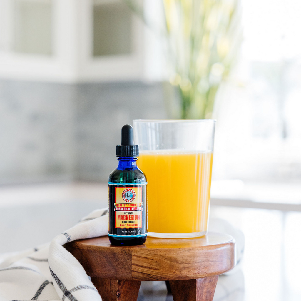 Bottle of G&G Tonic Water with Caffeine on a wooden table next to a glass of orange juice.