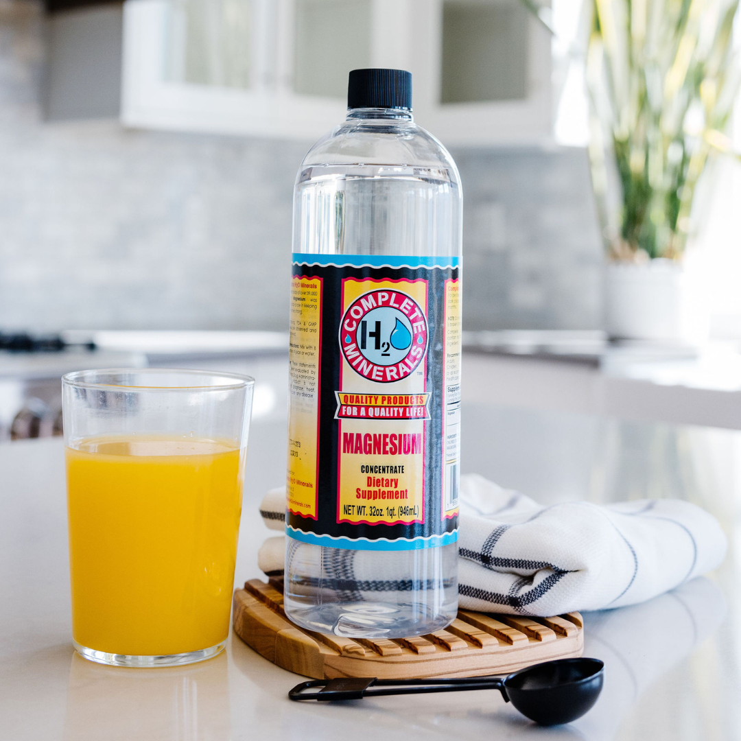 Bottle of Complete H2O Magnesium water on a kitchen counter with a glass of orange juice.