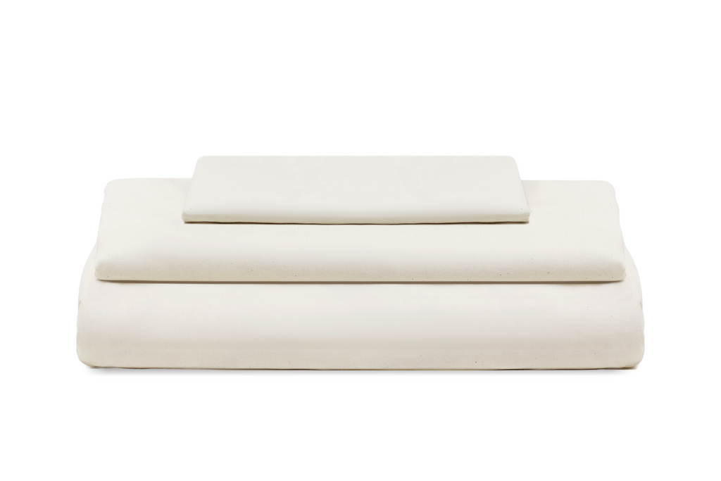 A stack of three folded sheets or bedding pieces in a solid off-white color, arranged neatly on a pure white background. Organic Sateen Bed Sheets Set